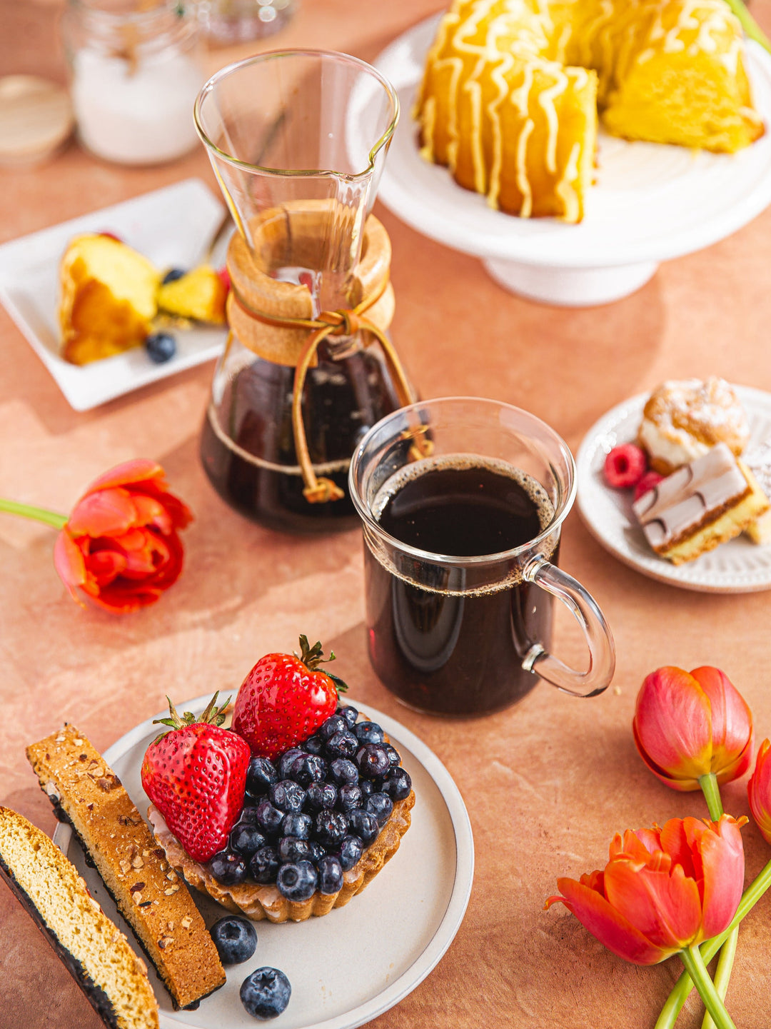 3-cup Chemex and full cup of coffee in the Murray mug on a table surrounded by flowers and pastries