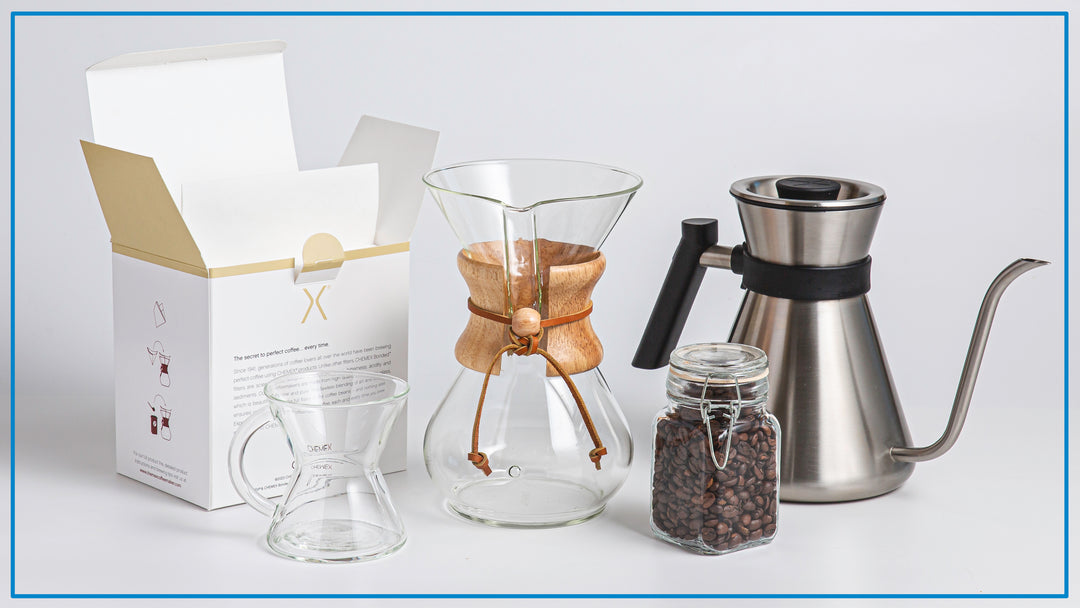 open box of filters, glass handle mug, 6-cup classic, container of coffee beans and the brushed chettle lined up against a light background