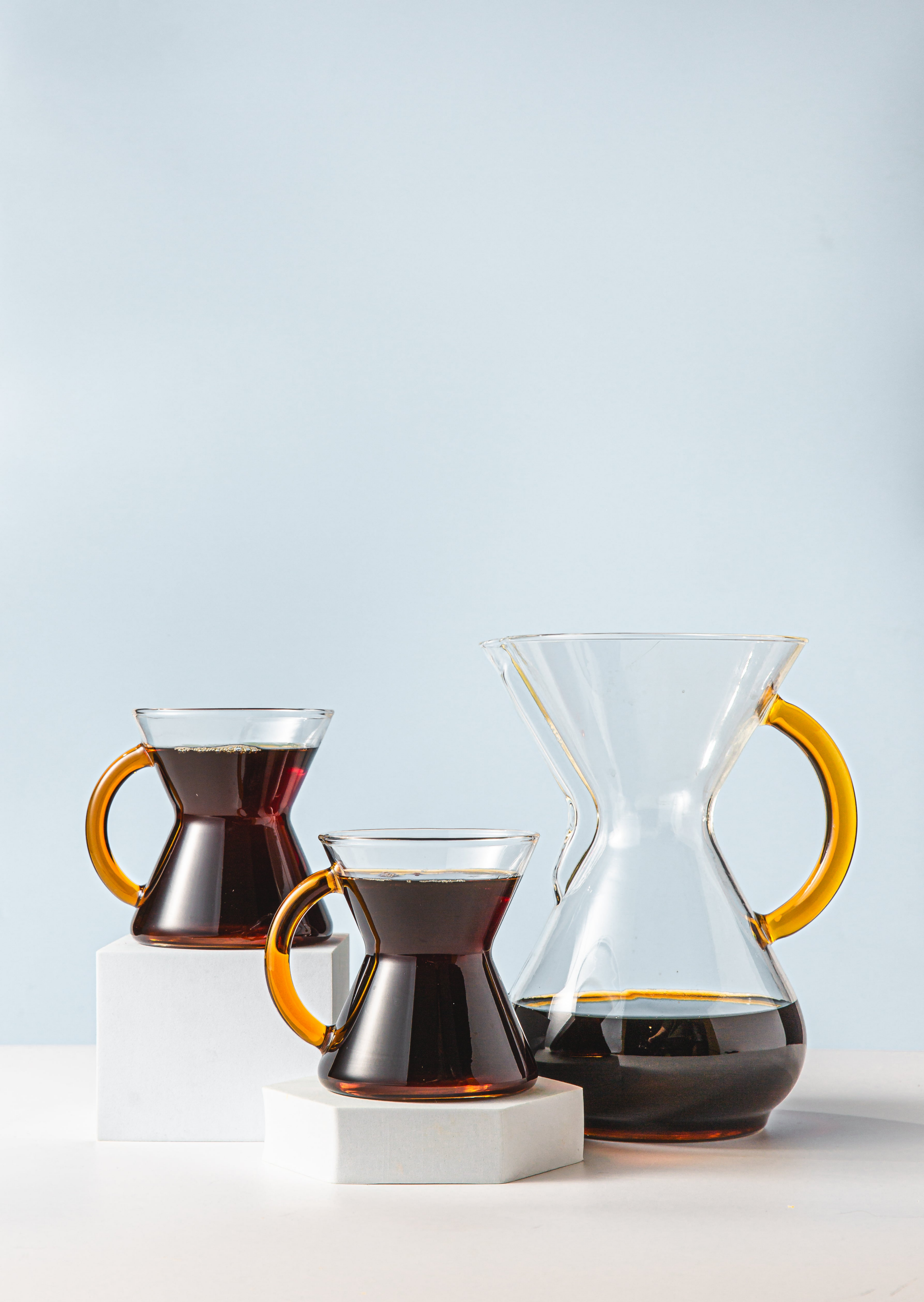 six cup gold glass handle set filled with coffee. 2 glass handle gold mugs and a 6-cup gold glass handle coffeemaker on a light blue background