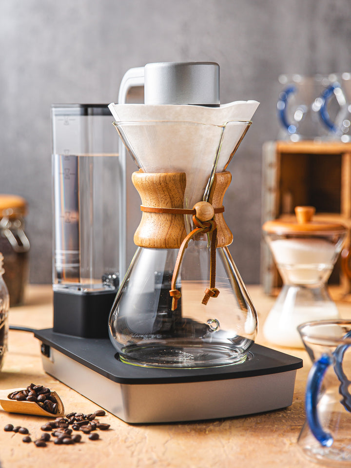 Ottomatic® 2.0 on a table with a chemex circle filter. in the background there are chemex sapphire glass handle mugs and a cream and sugar set