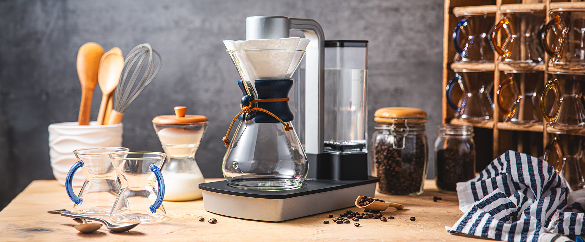 ottomatic coffeemaker with the 8-cup classic featuring a blue collar, sitting on a kitchen counter with glass handle mugs, cream and sugar set and coffeebeans