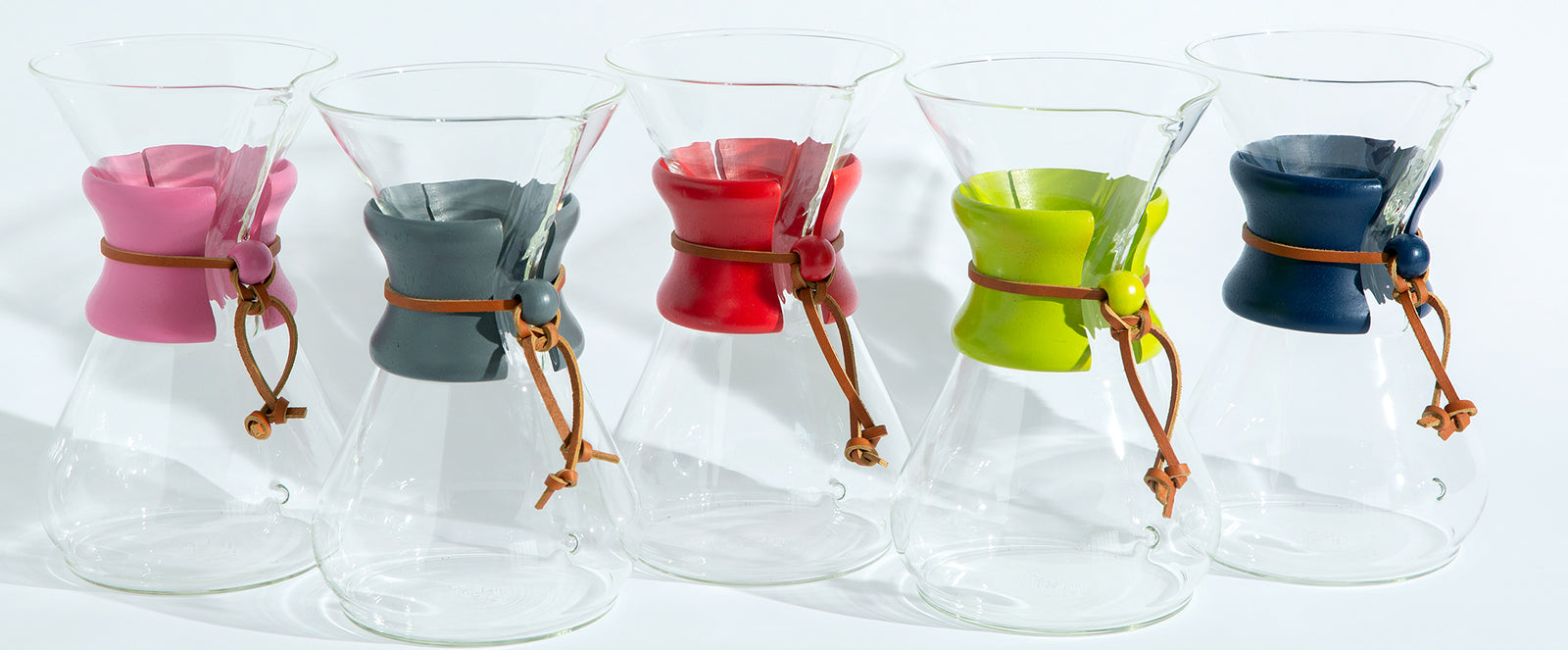 pink, grey, red, green and blue painted wooden collars tied on coffeemakers lined up on a white background