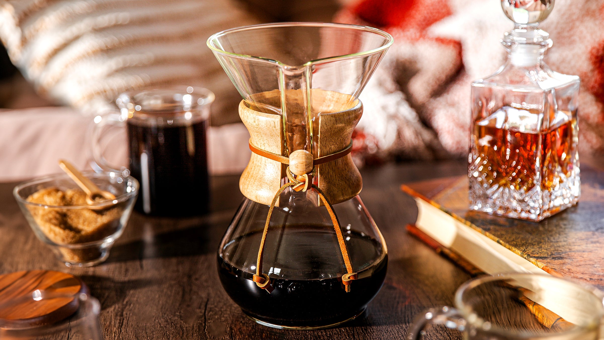 Chemex classic on a darker table top, in a front of a chair with a book and a liquor container. aklso featured the murray mu and the cream and sugar set