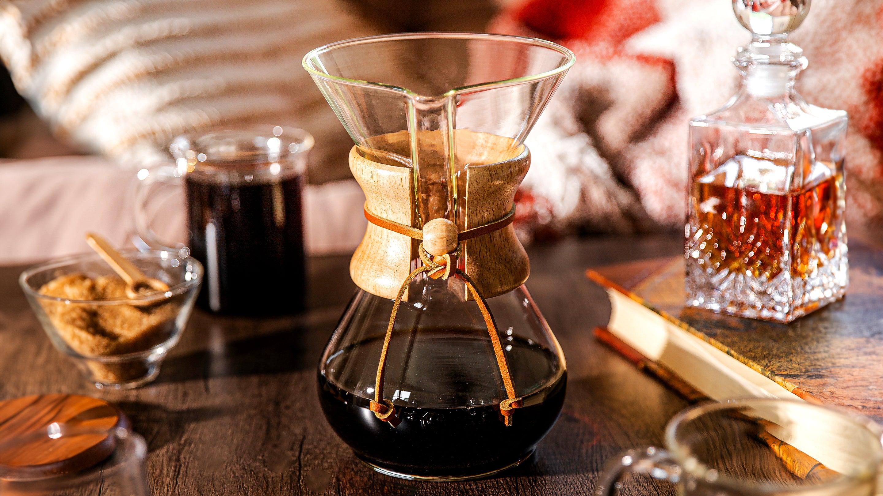 Chemex classic on a darker table top, in a front of a chair with a book and a liquor container. aklso featured the murray mu and the cream and sugar set