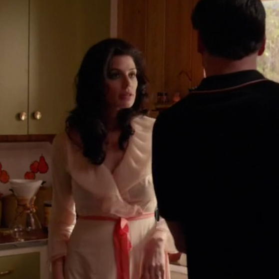 This image shows Jessica Paré as Megan Draper in Mad Men, wearing a beige Lucie Ann nylon dressing gown with a contrast ribbon tie and a chemex in the background 