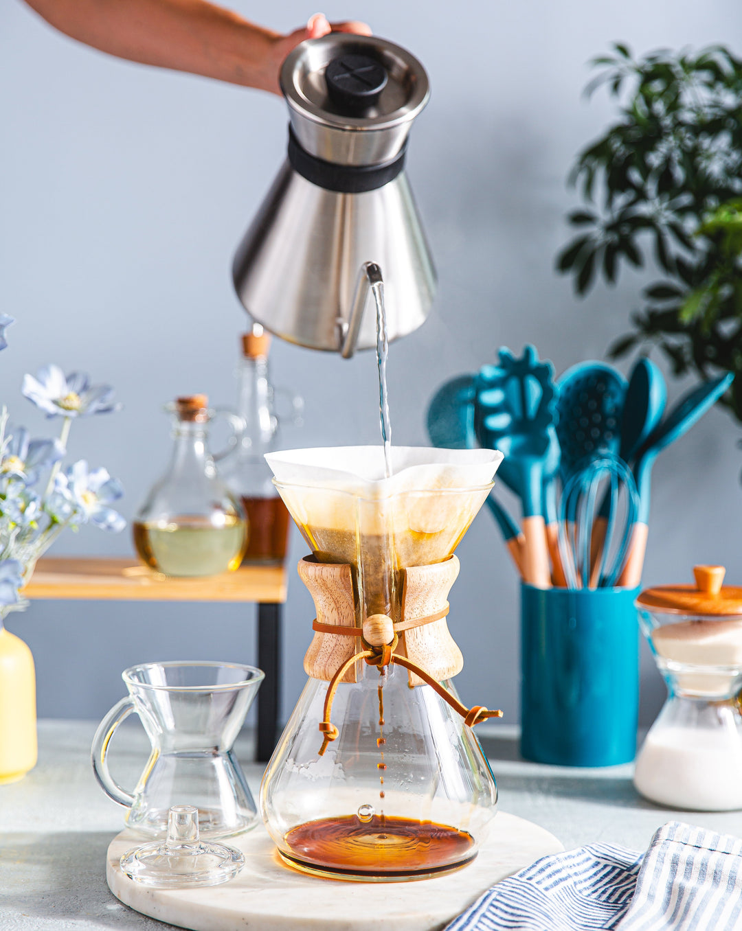 Person making coffee using a Chemex filter on a kitchen counter.