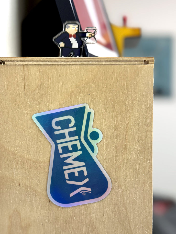 Chemex carafe holographic sticker stuck on a wooden surface with a blurred background