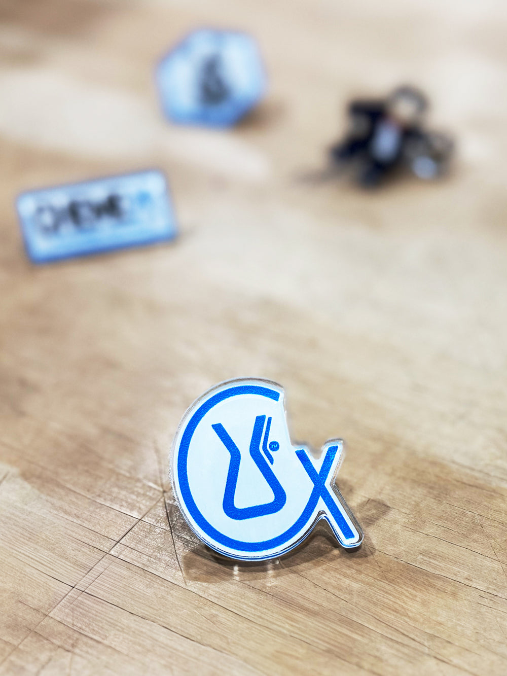 CX acrylic pin on a wooden table surface.