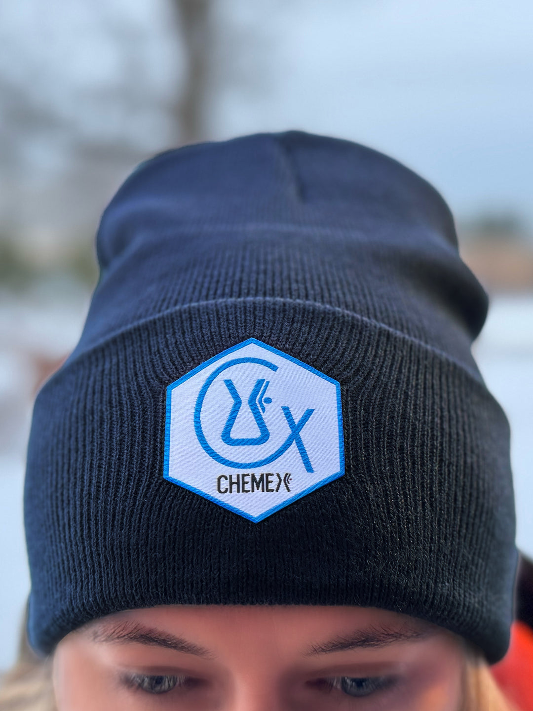 chemex chemist beanie with a blue and white Chemex logo patch worn by a person outdoors.