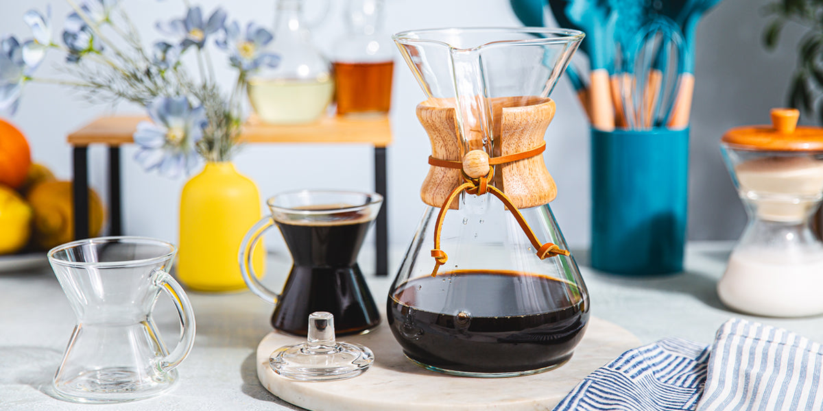 Coffee-making setup with a Chemex coffee maker on a table with various coffee-related items.