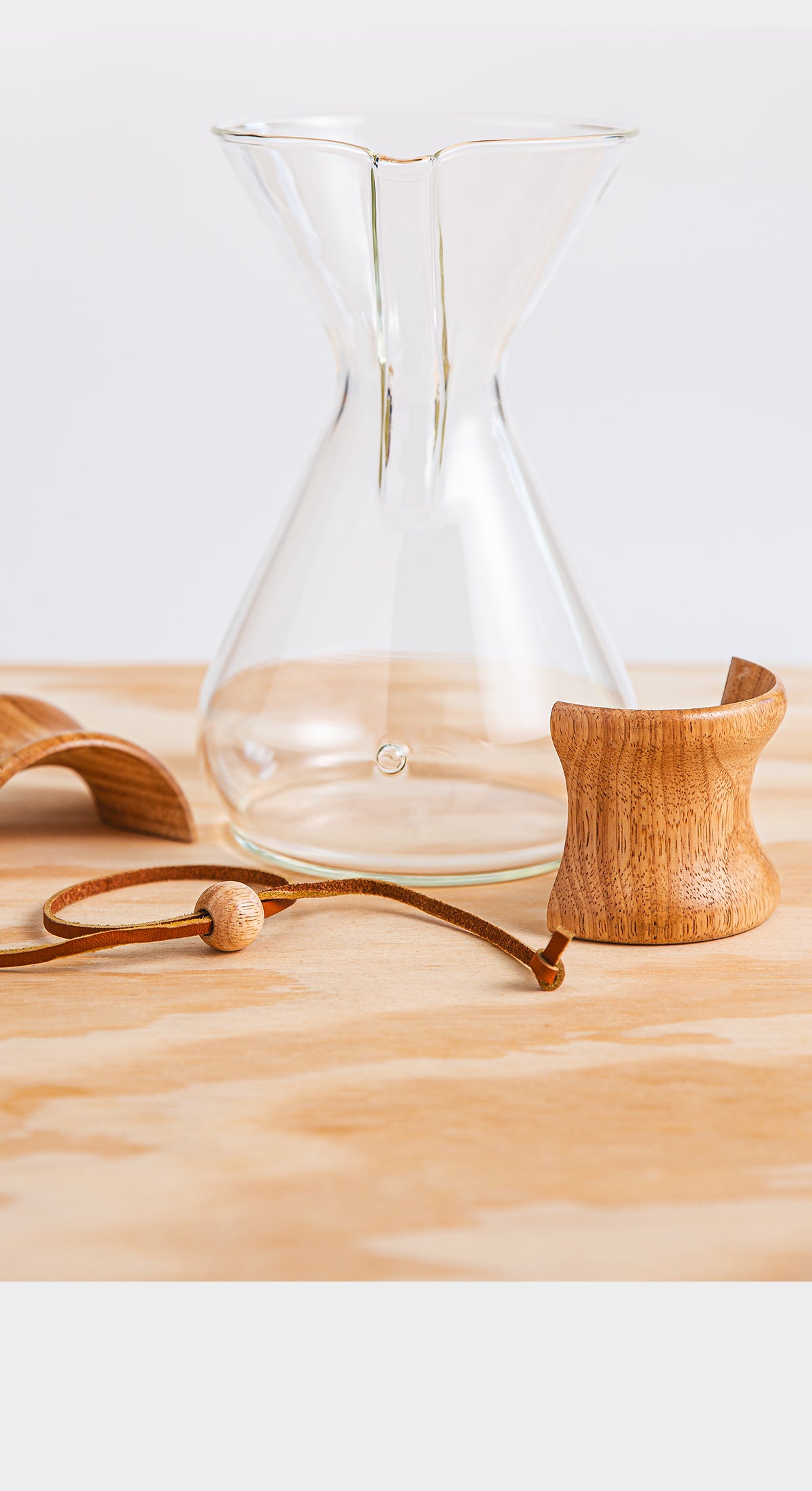 Glass coffeemaker with a wooden collar and rawhide sitting next to it untied.