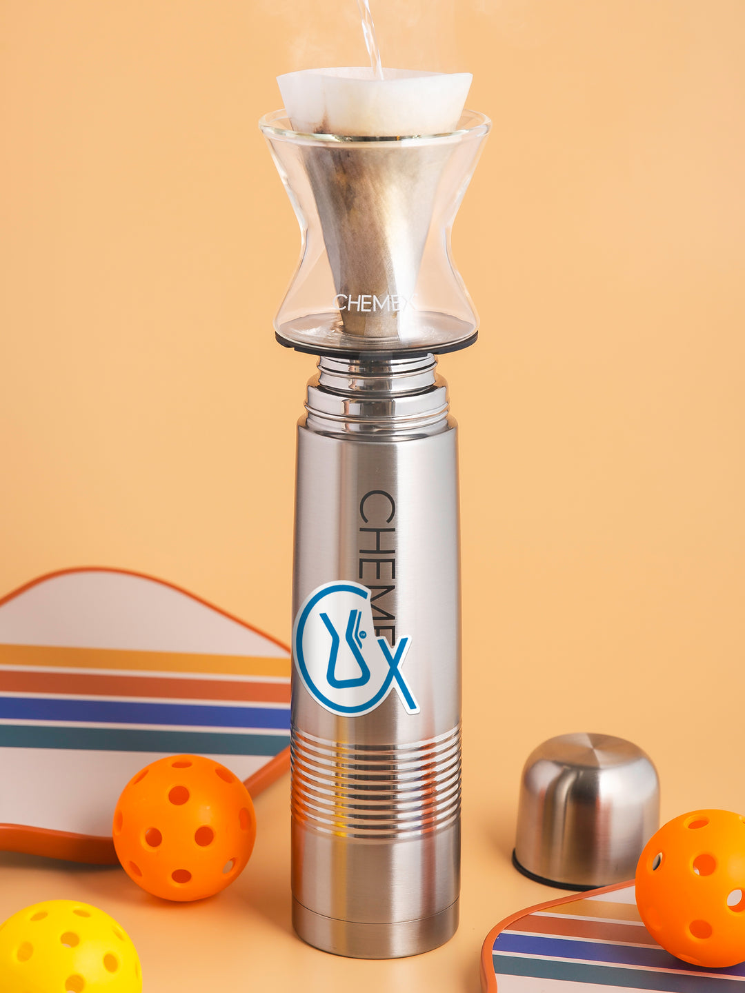 CX Symbol sticker stuck on a chemex thernos, surrounded by pickletball equipment. 