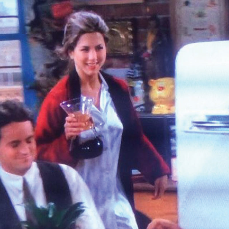 This image shows Jennifer Aniston as Rachel Green wearing a iconic red cardigan over a white button-down pajama shirt holding a chemex in the pilot episode of Friends 