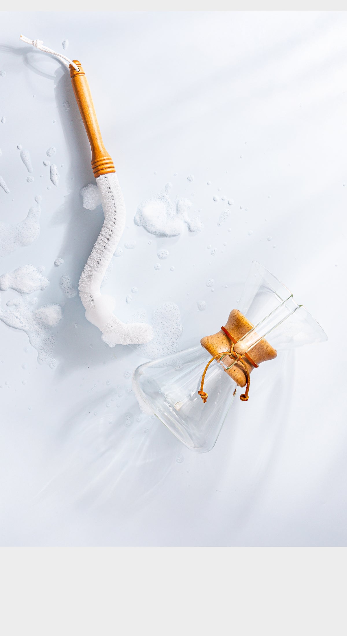 Chemex cleaning brush on a counter top with soup suds, next to them is a Chemex coffeemaker laying down. 