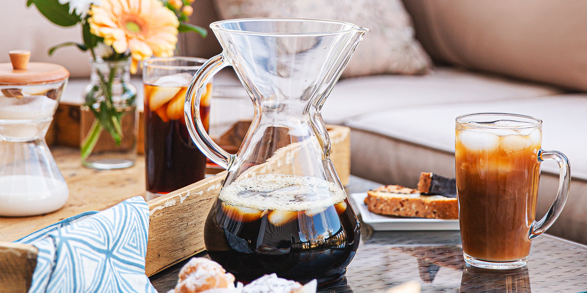 Coffee-making setup with a Chemex and a glass of iced coffee on a table.