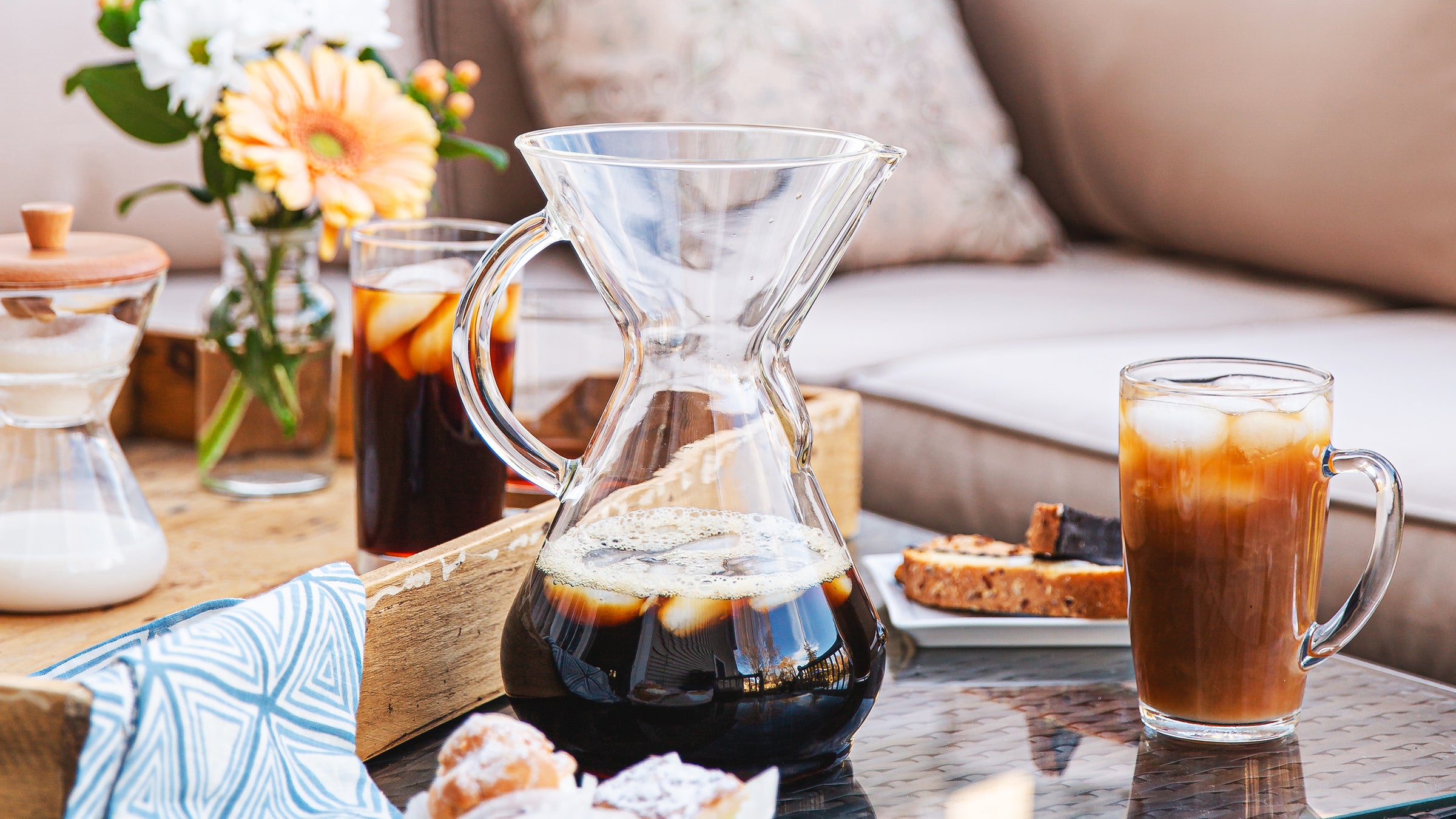 Glass carafe with coffee and a glass of iced coffee on a table with a cozy background.