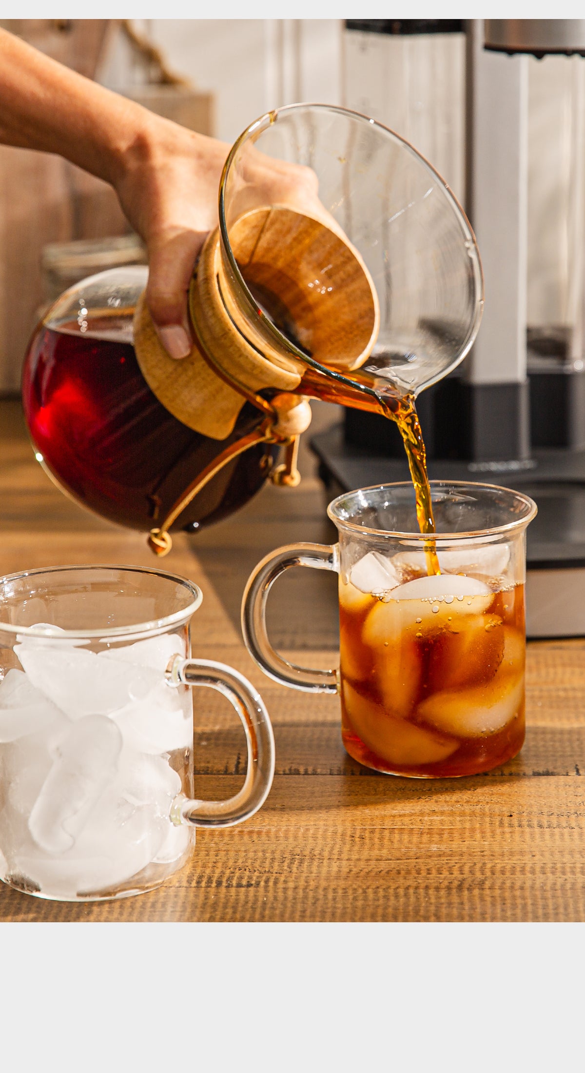 Pouring iced coffee from a glass carafe into a clear mug with ice cubes.