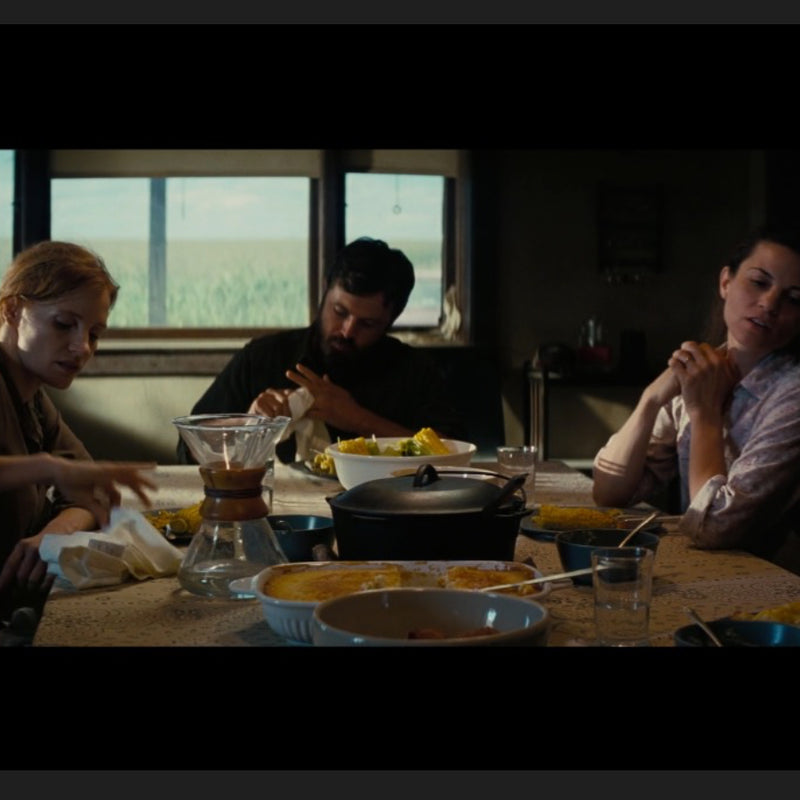 This image shows a scene from the film Interstellar featuring a Chemex glass coffee maker used as a water pitcher on a wooden dining table.