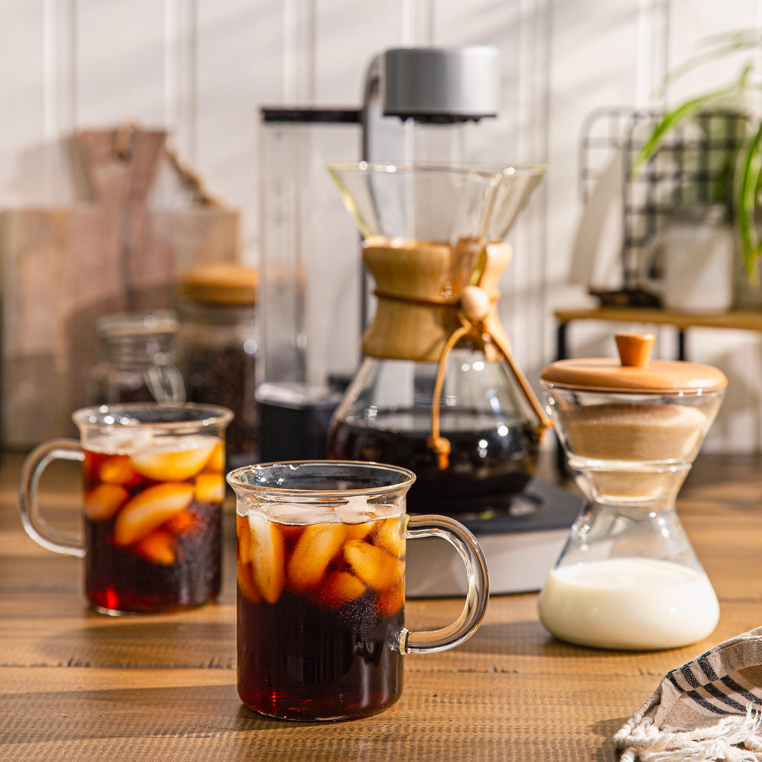 The chemex ottomatic brewed iced coffee, 2 murray mugs in front of the ottomatic filled with iced coffee, the cream and sugar set is stacked to the side.