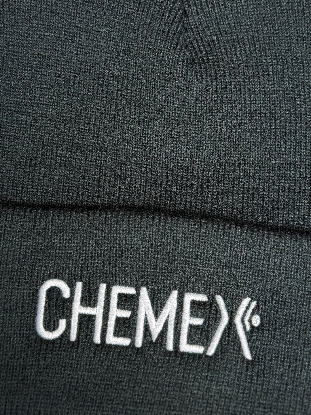 Close-up of a black beanie with 'CHEMEX' logo on a dark background