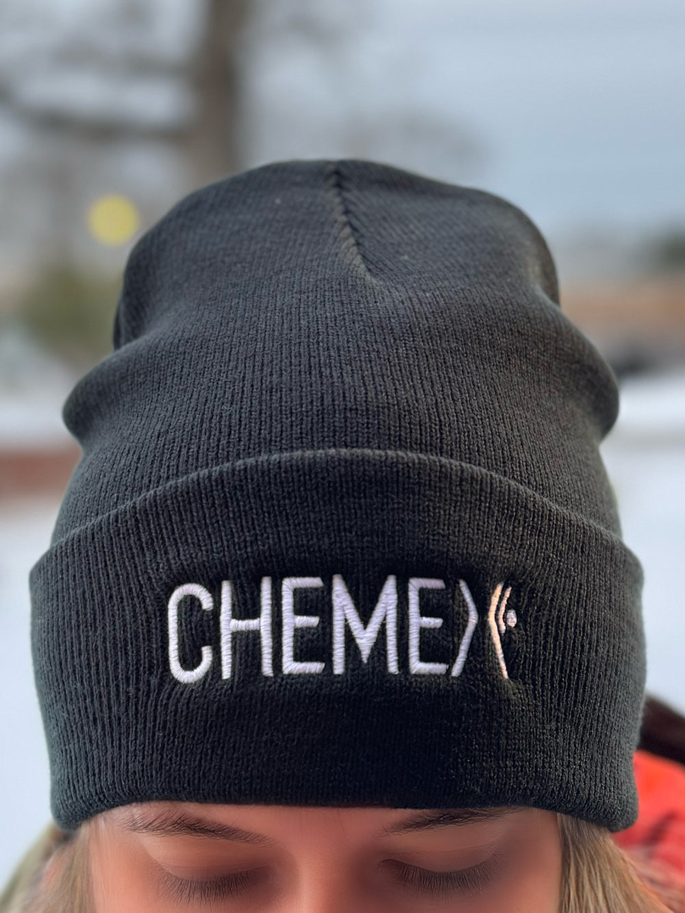 Black beanie with 'CHEMEX' logo worn by a person outdoors.