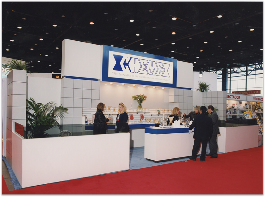 CHEMEX trade-show booth — large white-and-blue display with red-carpet floor, attendees inspecting products at the counter, 1990