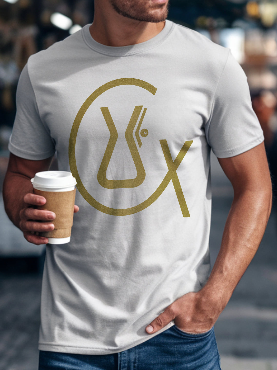 Person wearing a white t-shirt with a gold logo, holding a coffee cup.