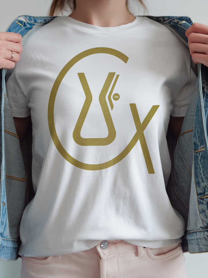 White t-shirt with gold logo worn by a person, with a denim jacket held open.